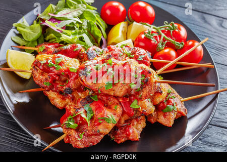 Chicken Döner Spezialitäten vom Holzkohlegrill auf Spieße mit Salat, Zitrone Keile auf einer schwarzen Platte, auf einem Holztisch, vertikale Ansicht von oben Stockfoto