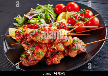 Chicken Kebab gegrillt auf Spieße mit Salat, Zitrone Keile auf einer schwarzen Platte, auf einem Holztisch, Ansicht von oben, cclose-up Stockfoto