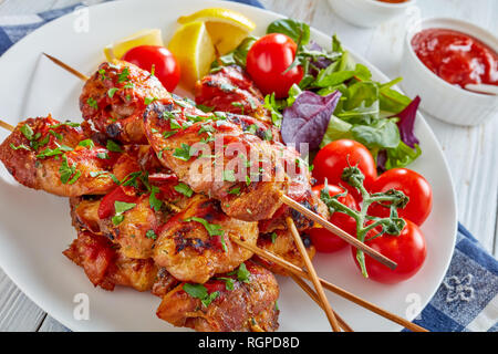 Chicken Döner Spezialitäten vom Holzkohlegrill auf Spieße mit Kräutern Salat, Tomaten, Zitrone Keile auf einer weißen Platte, auf einer hölzernen Tabelle, Ansicht von oben Stockfoto