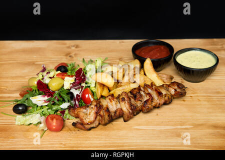 Closeup Stücke von lecker Gegrilltes Fleisch und verschiedene Gemüse in der Nähe der Schüssel liegend mit Tomatensauce auf hölzernen Tisch Stockfoto