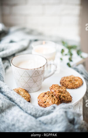 Gemütliche Wochenende Frühstück mit weißen Tasse Kaffee und Cookies auf Keramik Fach, warmes Licht home Inneneinrichtung closeup Stockfoto