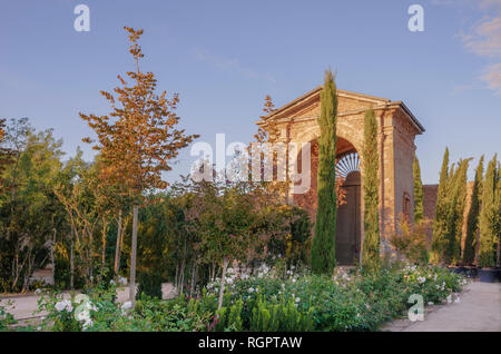 Ein Spanischer Garten mit Blumen an der Grenze einen Weg zu einem dekorativen Bogengang. Eine Mauer ist auf der Rückseite und ein blauer Himmel ist oben. Stockfoto