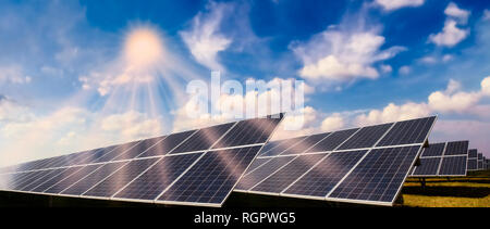 Photovoltaikanlage mit Solarmodulen und helle Sonne vor blauem Himmel Stockfoto
