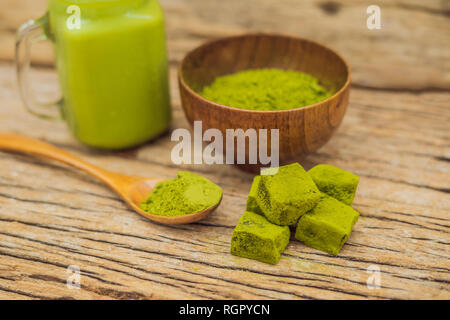 Grüner Tee Latte mit Eis im Marmeladenglas, Matcha Pulver und Süßigkeiten aus Matcha auf Holz- Hintergrund. Hausgemachte Eistee Matcha Latte Tee mit Milch Null Stockfoto