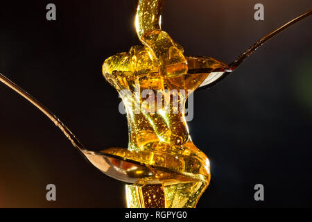 Honig mit Gold Farbe fließt unten von einem Löffel, auf einem dunklen Hintergrund. Das gesunde Essen. Diät. Selektive konzentrieren. Stockfoto