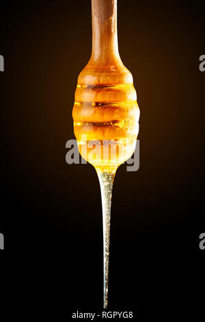 Honig mit Gold Farbe fließt unten von einem Löffel, auf einem dunklen Hintergrund. Das gesunde Essen. Diät. Selektive konzentrieren. Stockfoto