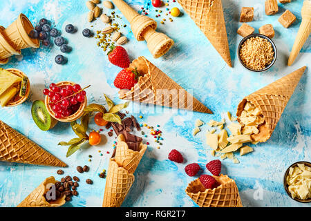 Knusprige Waffel Kegel mit Obst und süßen Zutaten vor blauem Hintergrund Stockfoto