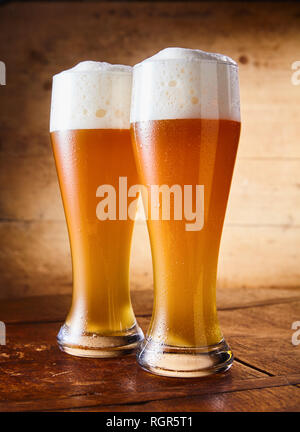 Zwei große elegante pint Gläser kaltes Weißbier mit einer schaumigen Kopf auf einer Bar aus Holz Tisch konzeptionellen der Oktoberfest Stockfoto
