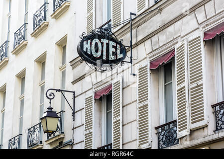 Das abgenutzte schmiedeeiserne Zeichen eines bescheidenen Hotels an der Fassade eines alten Gebäudes mit einer alten Straßenbeleuchtung in einem Touristenviertel von Paris. Stockfoto