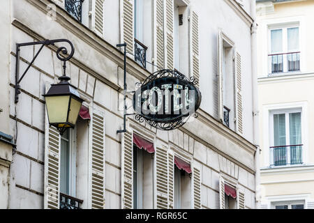 Das abgenutzte schmiedeeiserne Zeichen eines bescheidenen Hotels an der Fassade eines alten Gebäudes mit einer alten Straßenbeleuchtung in einem Touristenviertel von Paris. Stockfoto