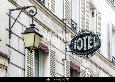 Das abgenutzte schmiedeeiserne Zeichen eines bescheidenen Hotels an der Fassade eines alten Gebäudes mit einer alten Straßenbeleuchtung in einem Touristenviertel von Paris. Stockfoto