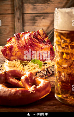 Gebratene Schweinshaxe mit Sauerkraut serviert mit einem kalten schaumiges Bier und Brezel in einer rustikalen Taverne am Oktoberfest Stockfoto