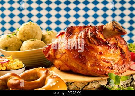 Eine knusprig gebratene Schweinshaxe serviert auf einem urigen Holzblock mit großzügigen gourmet Beilagen. Stockfoto