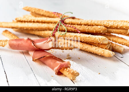 Frisch gebackene italienische grissini Brot Sticks in Schinken auf einem high key Holz Hintergrund gewickelt. Stockfoto