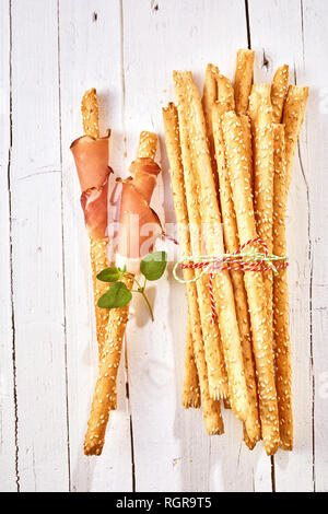 Knusprig gebackene italienische grissini Brot Sticks in Schinken gewickelt und mit frischen Kräutern auf einem high key Holz Hintergrund garniert. Stockfoto