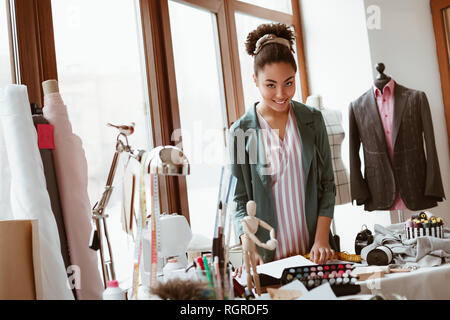 Keine Zeit, um sich zu entspannen. Junge schöne afrikanische Frau Schneider steht in der Nähe von Vorhängen und Modellierung neue Kleidung im Design Studio Stockfoto