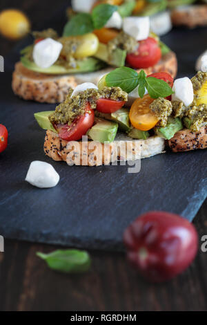 Avocado toast Sandwich mit Avocados, Pesto, Mozzarella, frisch aus dem Garten Basilikum und heirloom Tomaten, über eine rustikale Holz- Hintergrund. Stockfoto