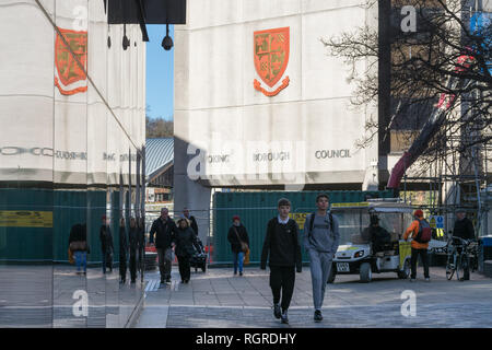 Das Büro des Woking Borough Council spiegelt sich in den Fenstern eines angrenzenden Gebäudes mit Leuten, die vorbeilaufen, in Surrey, England, Großbritannien Stockfoto