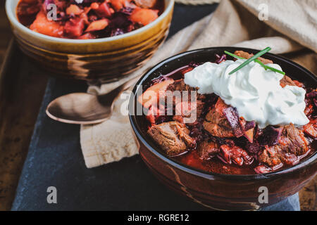 Zwei Schalen mit Borscht Suppe mit herzhaften, fleischigen Brocken von Rindfleisch, Wurzelgemüse, Kraut und Rüben. Mit saurer Sahne und Schnittlauch serviert, hohe Blickwinkel betrachten. Stockfoto