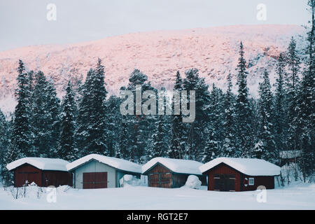 Kleine Scheunen in der Nähe von Nadelbäumen und Berg im majestätischen arktischen Landschaft im Winter Tag Stockfoto