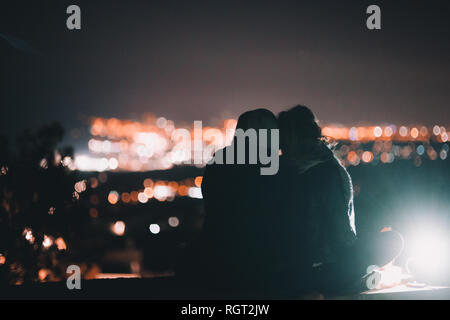 Rückansicht eines jungen Mannes und einer Frau, die sich umarmen und die wunderbare Nachtstadt bewundern Stockfoto