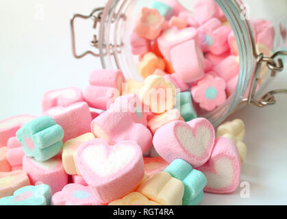 Haufen von Pastelltönen in Herzform und mit Blumen geformte Marshmallow Süßigkeiten verteilt aus Glas auf weißer Tisch, Valentine, Konzept Stockfoto