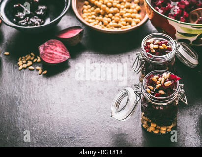 Gesund vegan Rote-Bete-Salat mit Kichererbsen und Pinienkerne in Gläser für Mittagessen auf dunklen Küche Tisch Hintergrund mit Zutaten, Ansicht von oben. Lila veg Stockfoto