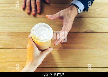 Barista serviert Kaffee zu einem Mann. Hand Pappbecher Kunststoffkappe Holztisch Pause Blazer. Kaffeepause Konzept Stockfoto