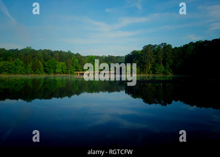Einen malerischen Blick über die noch Wasser mit Spiegel - wie Himmel und Baum Reflexionen an Shelley See Park in Raleigh, North Carolina. Stockfoto
