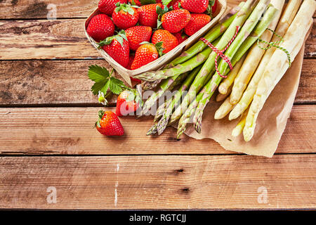 Bündel von frischen, rohen weißen und grünen Spargelspitzen mit einem kleinen Behälter an reife Saftige Erdbeeren auf einem Holztisch mit Kopie der Platz in einem hohen Stockfoto