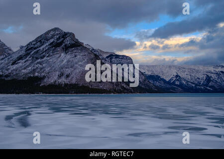 Bewölkt bunten Himmel und im Winter Sonnenuntergang über berggipfel am Lake Minnewanka, Banff National Park, Alberta, Kanada, 2018 Stockfoto