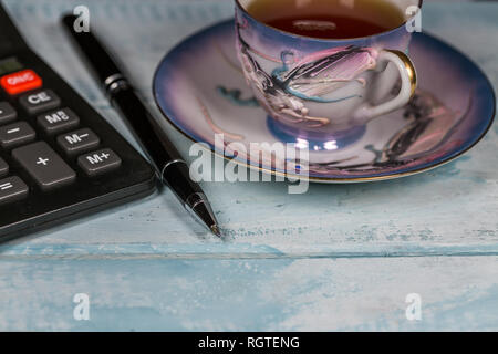 Taschenrechner, Stift und Tasse Tee auf dem hölzernen Tisch Stockfoto