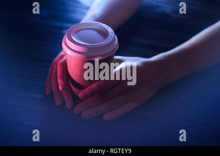 Eine Tasse Kaffee auf einen hölzernen Tisch in weibliche Hände. Pappbecher Kunststoffkappe schöne Hände Mädchen Theke Licht Stockfoto