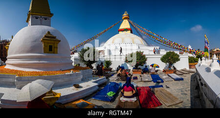 Panoramablick auf den großen Stupa mit flatternden Gebetsfahnen in Boudha, tibetischen Pilgern üben Niederwerfungen unten Stockfoto