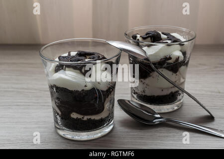 Zwei köstliche hausgemachte Joghurts von Schokolade und Sahne in einem Glas mit zwei Löffeln auf einem Holztisch Stockfoto