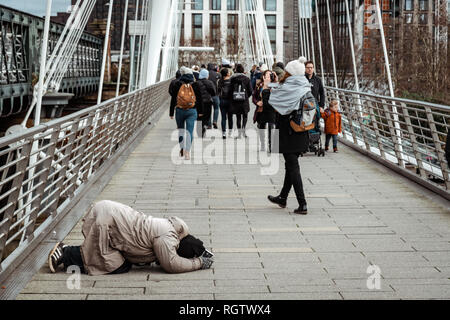 London, UK, 26. Januar 2019: Obdachlosen in einem betenden Position, betteln auf Hungerford Bridge in der Nähe von Waterloo Station, London Stockfoto