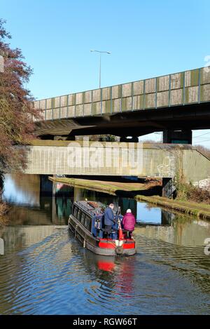 Ein schmales Boot auf der Kreuzung der Wey Navigation und der Basingstoke Canal an New Haw, mit erhöhten Abschnitt der Autobahn M25, Surrey, England Stockfoto