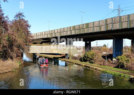 Ein schmales Boot auf der Kreuzung der Wey Navigation und der Basingstoke Canal an New Haw, mit erhöhten Abschnitt der Autobahn M25, Surrey, England Stockfoto