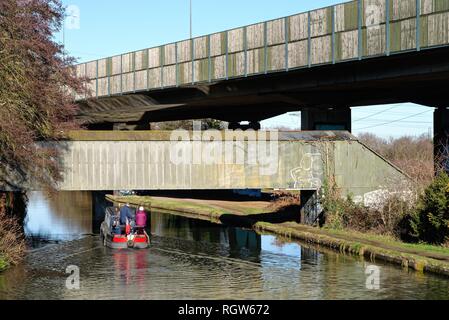 Ein schmales Boot auf der Kreuzung der Wey Navigation und der Basingstoke Canal an New Haw, mit erhöhten Abschnitt der Autobahn M25, Surrey, England Stockfoto