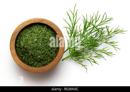 Getrocknete gehacktem Dill in einem dunklen Holz Schüssel neben frischen Dill Blätter auf Weiße von oben isoliert. Stockfoto