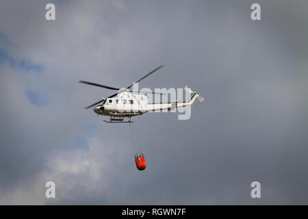 Die Brandbekämpfung Helikopter mit Bambi Korb mit Wasser auf dem Weg zu einem Brand geladen Stockfoto