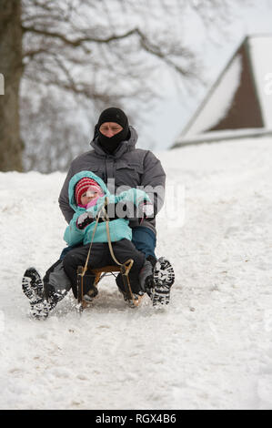 Vater und Sohn reiten Schlitten bergab Stockfoto