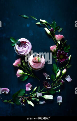 Cupcakes mit Erdbeeren und rosa Blüten auf einem dunklen Hintergrund. Feder dessert Konzept mit Kopie Raum Stockfoto