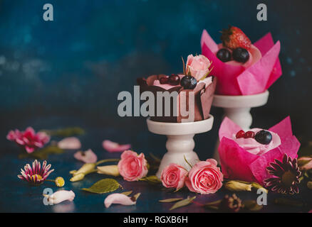 Cupcakes mit auf Porzellan steht mit rosa Blüten auf einem dunklen Hintergrund. Feder dessert Konzept mit Kopie Raum Stockfoto