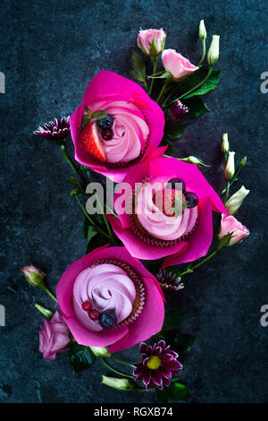 Cupcakes mit rosa umhüllt und rosa Blüten auf einem dunklen Hintergrund. Feder Dessert für drei mit Kopie Raum Stockfoto