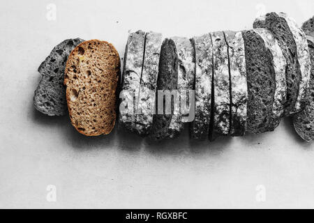Ein Laib Brot auf einem weißen Tisch, in Scheiben geschnitten, in Schwarz und Weiß, Monochrom. Stockfoto
