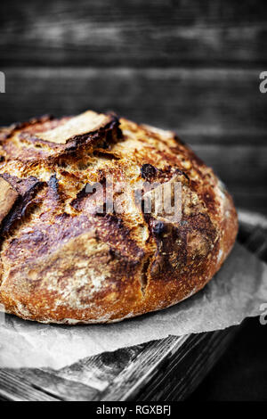Ein Laib Brot auf einem Tisch, an einem Tisch mit einem hölzernen Wand dahinter, in Schwarz und Weiß, Monochrom. Stockfoto
