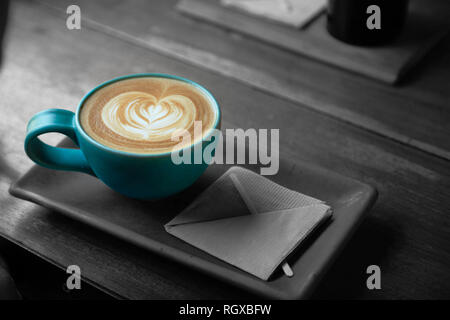 Eine Tasse Kaffee mit einem Herzen latte Schaum Kunst auf, sitzen auf einem rechteckigen Untertasse und auf einem Holztisch, in Schwarz und Weiß, Monochrom. Stockfoto