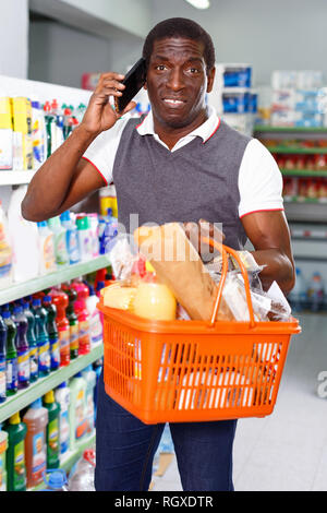 Positive heiter lächelnd afro Mann mit seinem Smartphone beim Einkaufen im Supermarkt Stockfoto