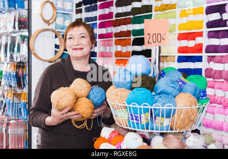 Froh, heiter, reife Frau kaufen bunte Garne für Ihr Hobby auf spezielle Angebote Stockfoto